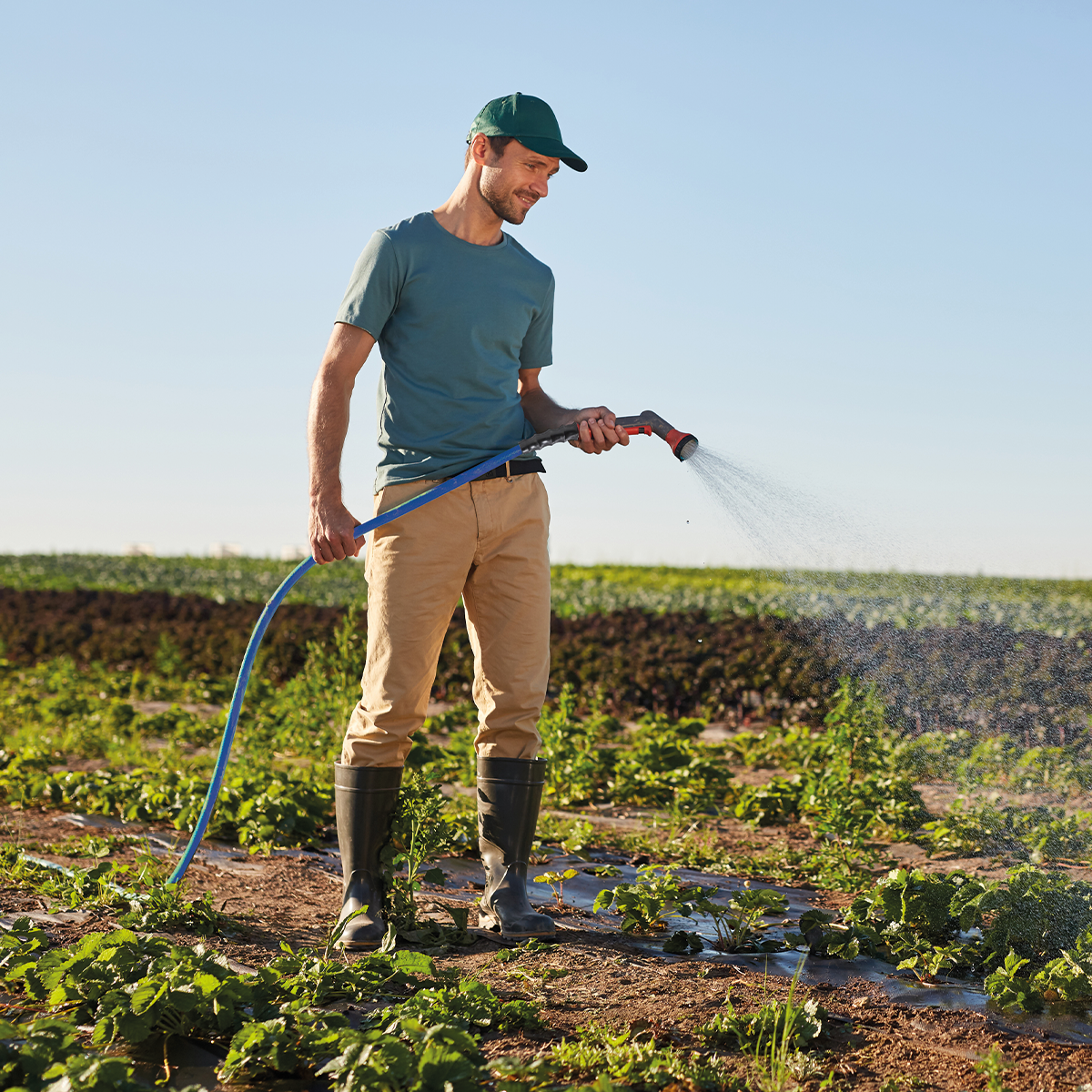 A man using irrigation hose to spray water on field.